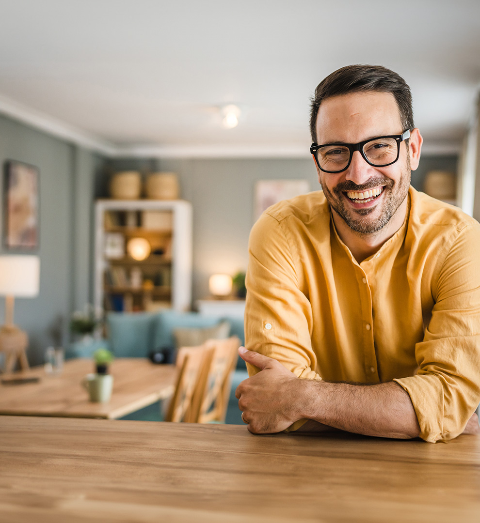 Man in a yellow sweater with arms crossed in a living room setting.