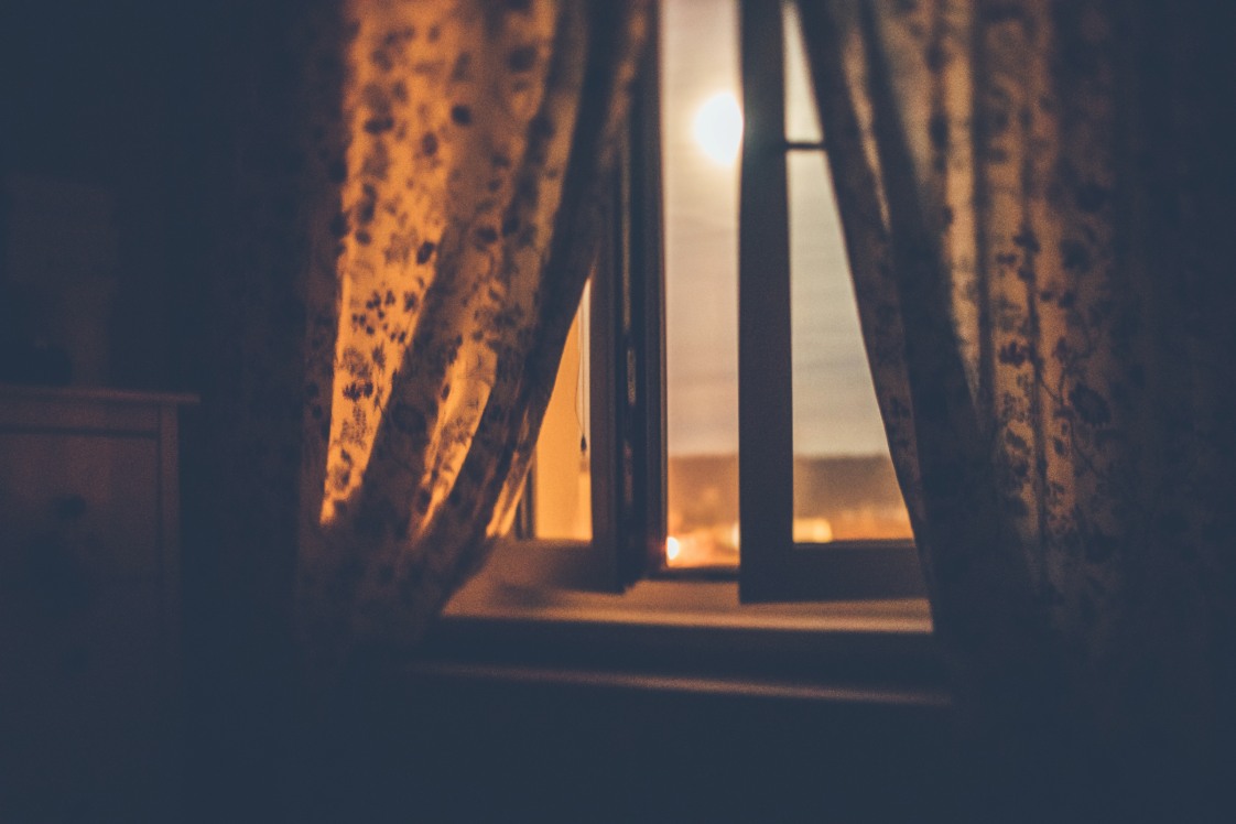 Visual of the moon through a curtained window at night.