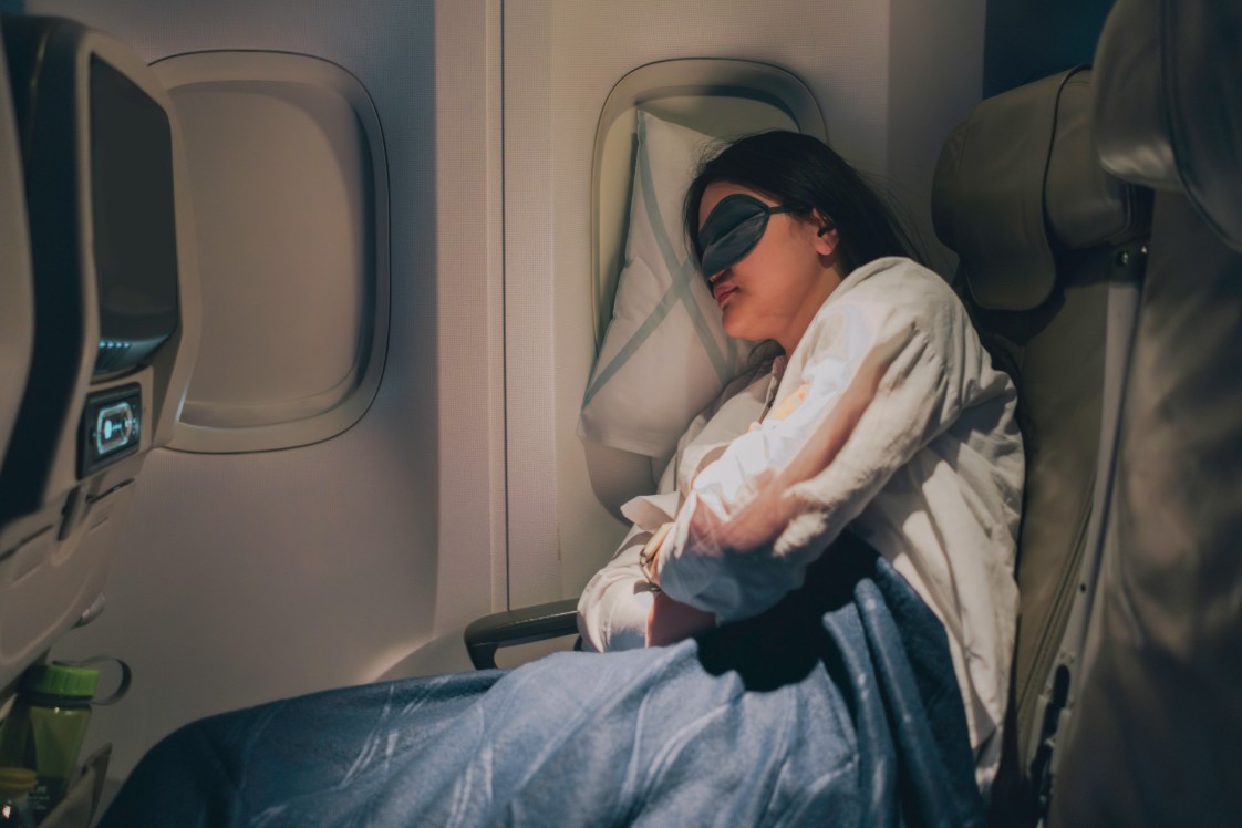 A person  sleeping on an airplane with a blue blanket.