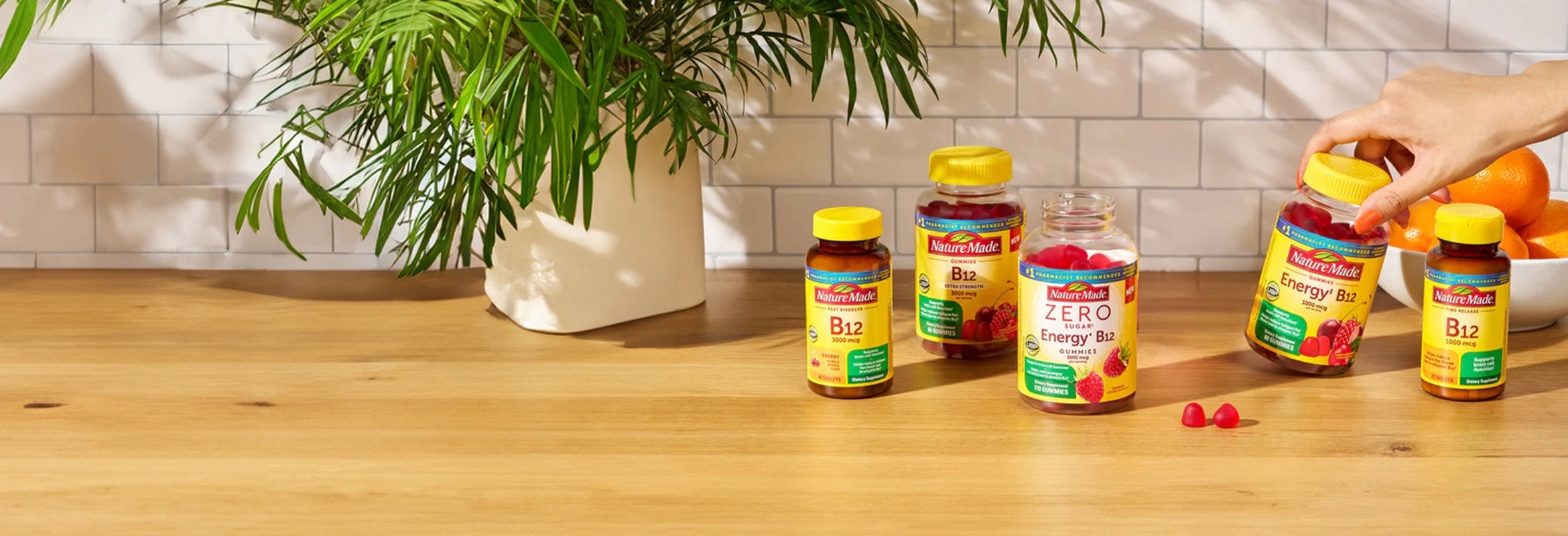 Hand reaching for a Nature Made B Vitamin supplement bottle and two gummies on a table.
