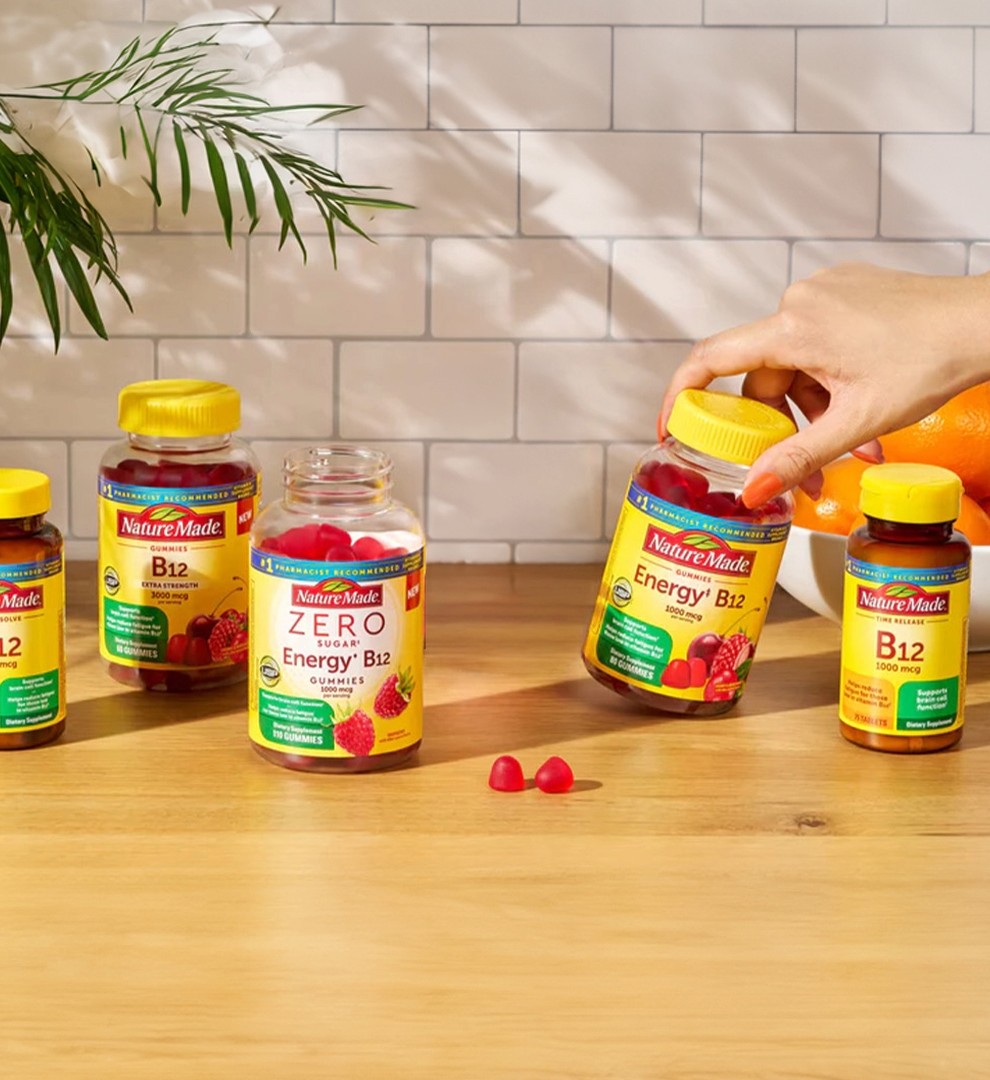 Hand reaching for a Nature Made B Vitamin supplement bottle and two gummies on a table.