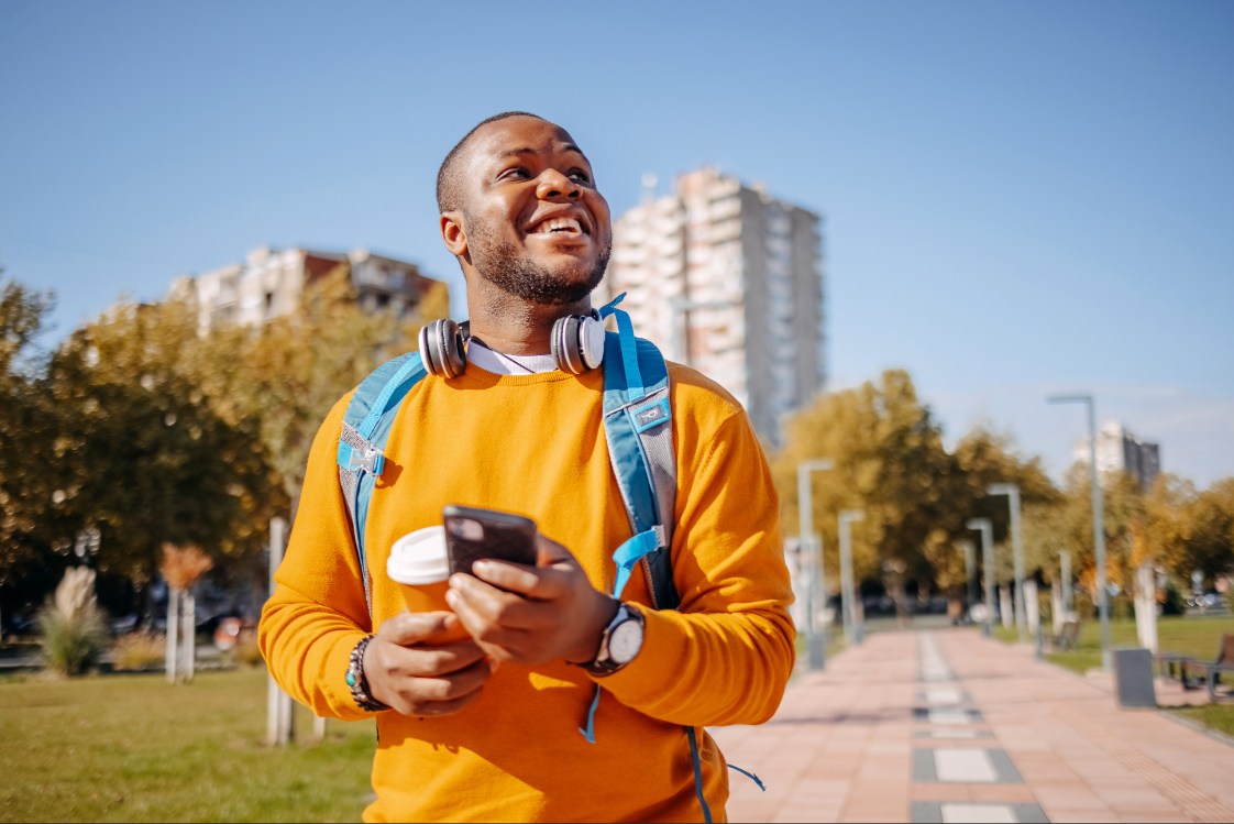 Young adult using a smartphone while walking through a city park on a sunny day.