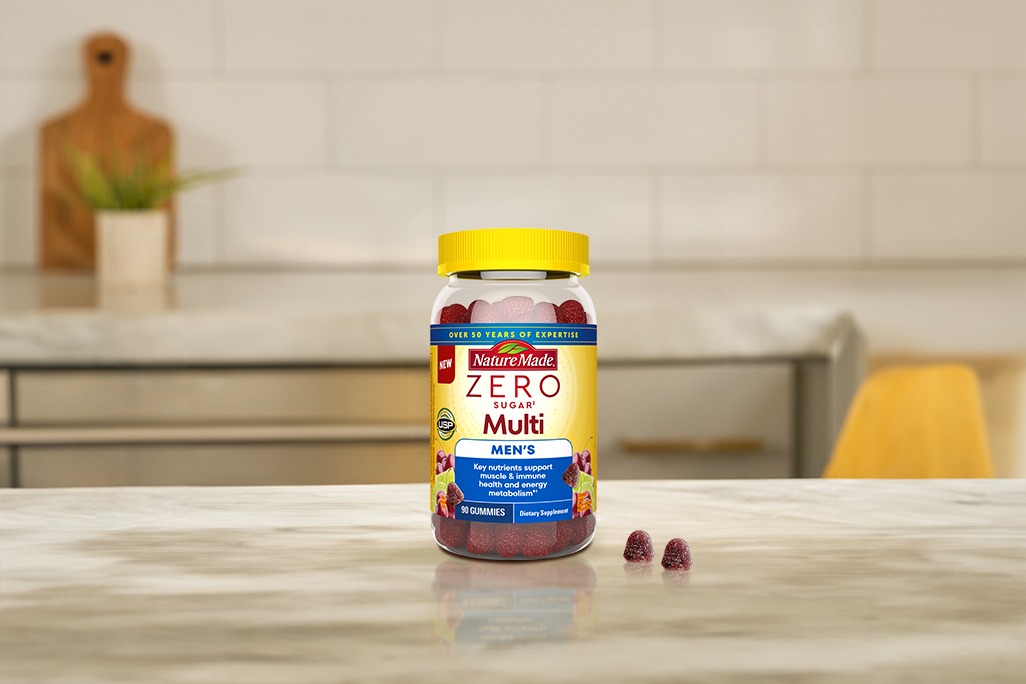 Nature Made Zero Sugar Men's Multivitamin Gummies with two gummies beside it on a kitchen counter. 