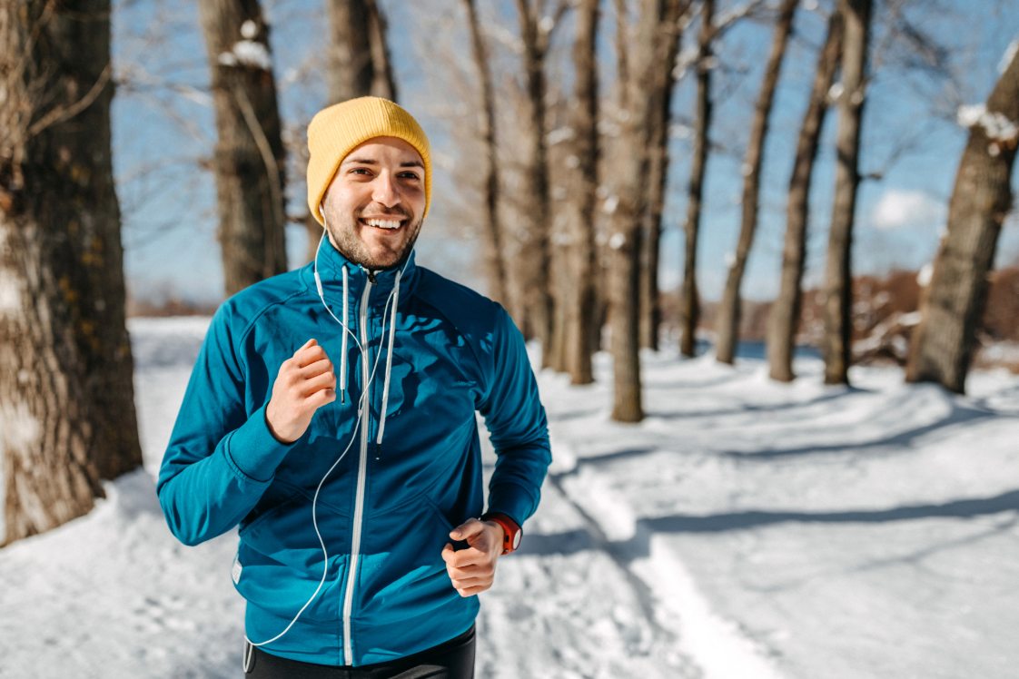 Runner jogging along a snowy park trail with trees in the background