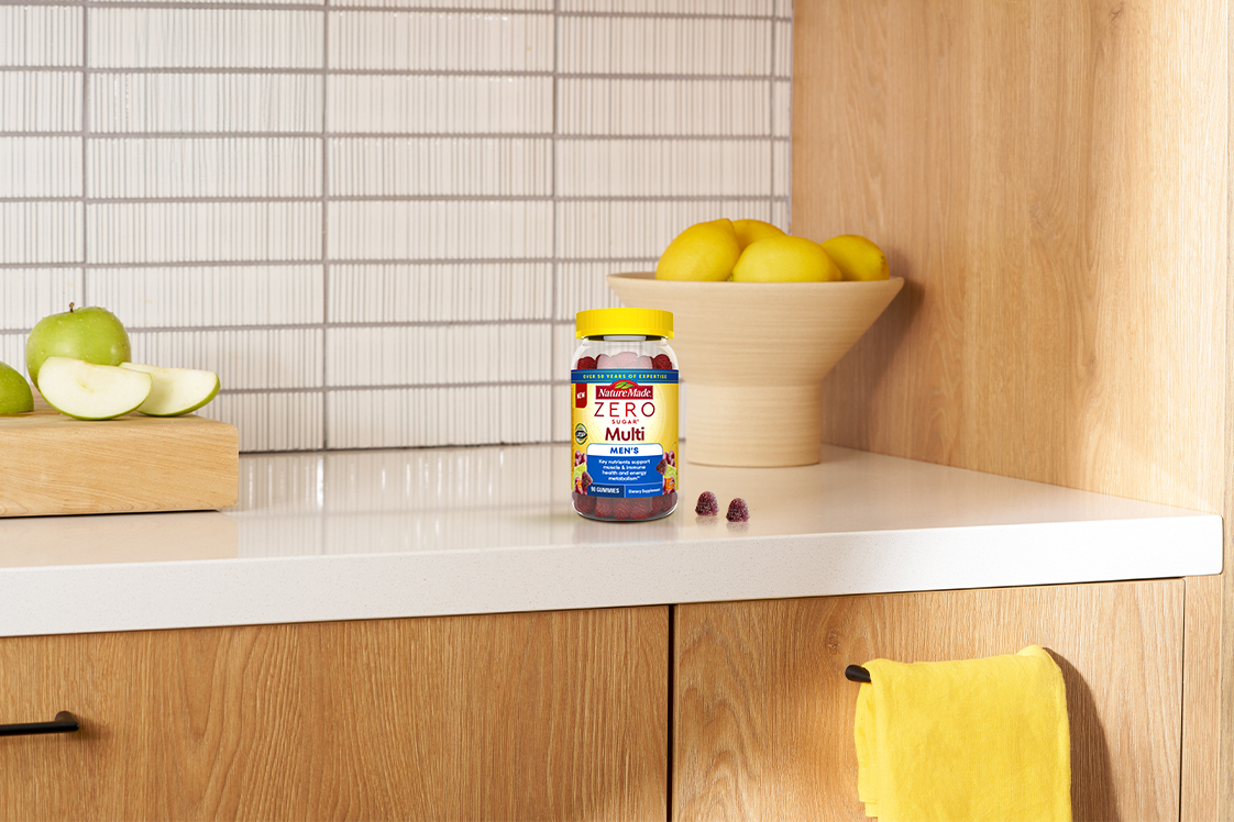 Nature Made Zero Sugar Men’s Multivitamin gummies on a kitchen countertop with fresh fruit.