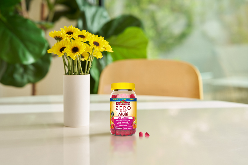 Nature Made Zero Sugar Women’s Multivitamin gummies on a bright table with yellow flowers.