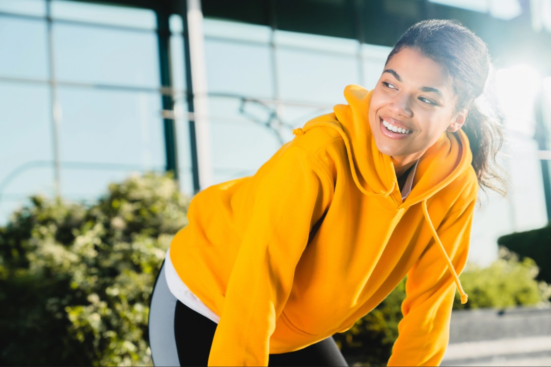 Person stretching outdoors in a yellow hoodie before a fitness workout.