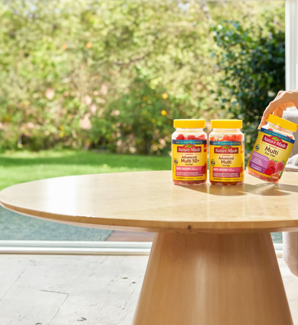 Nature Made multivitamin supplements arranged on a wooden table in a bright, sunlit home setting.