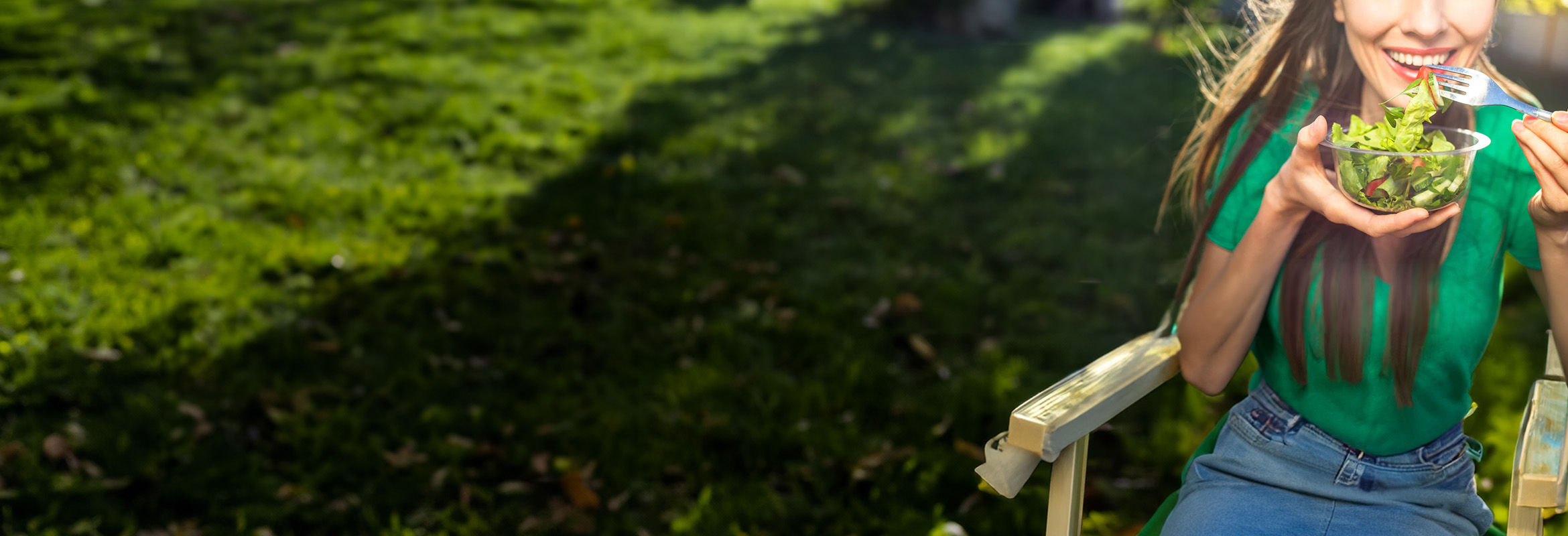 Person enjoying a fresh green salad outdoors on a sunny day.