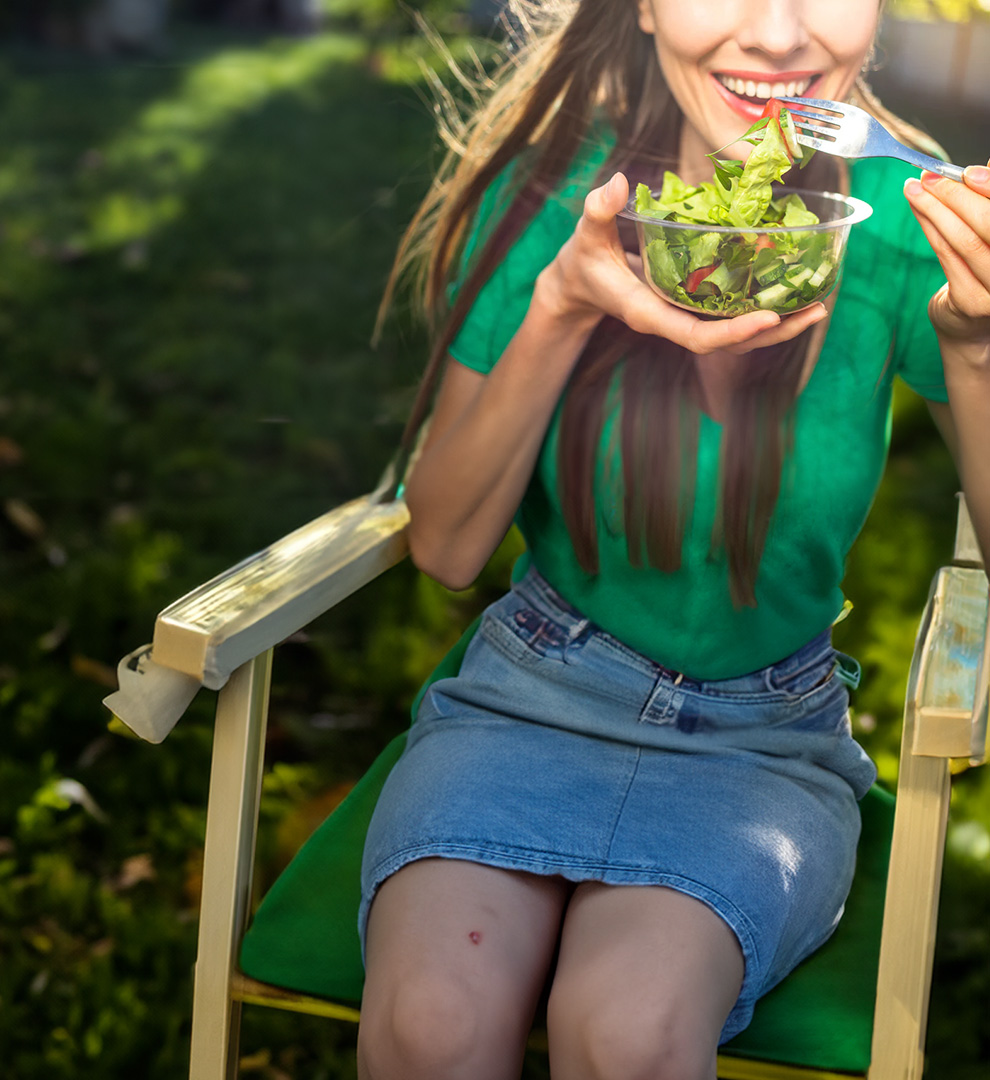 Person enjoying a fresh green salad outdoors on a sunny day.