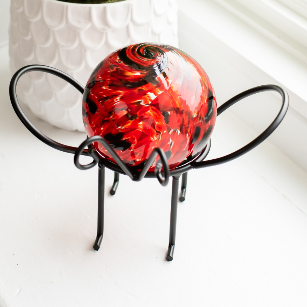 Black and red glass orb on a black insect garden holder on a white window sill