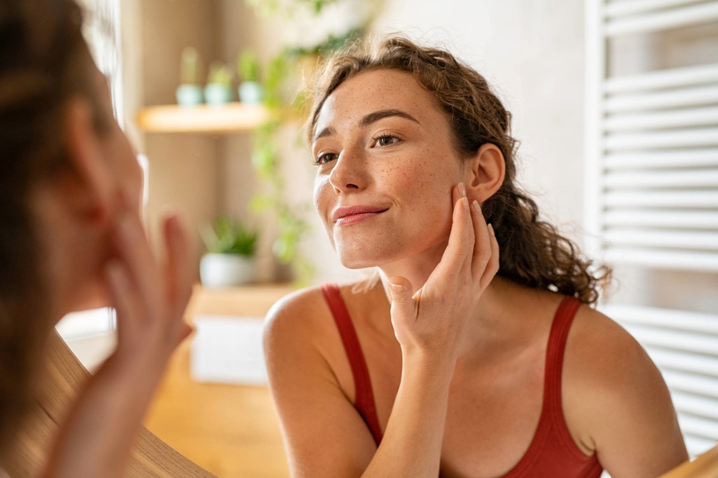 Person touching cheek while checking skin in a sunlit room.