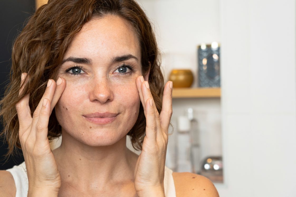Person gently touching face in a bright bathroom.