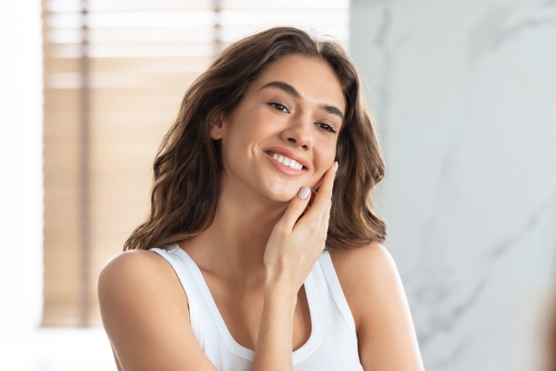 Person smiling while touching their face and looking in bathroom mirror.