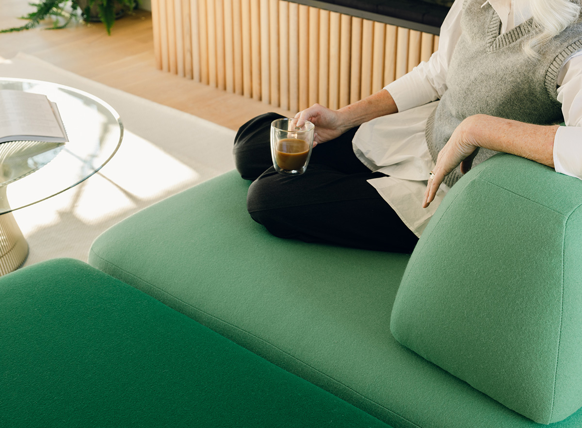 Image: A close up of a woman sitting comfortable on a green Floyd Magna sectional in a brightly lit room with wood floors