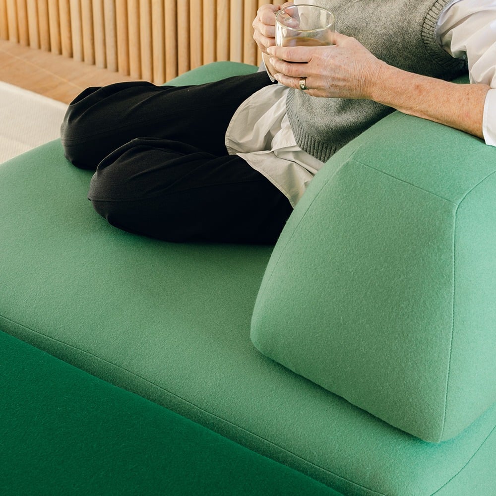 Image: A close up of a woman on a Green Floyd Magna sectional. She is holding a drink and sitting comfortably. 