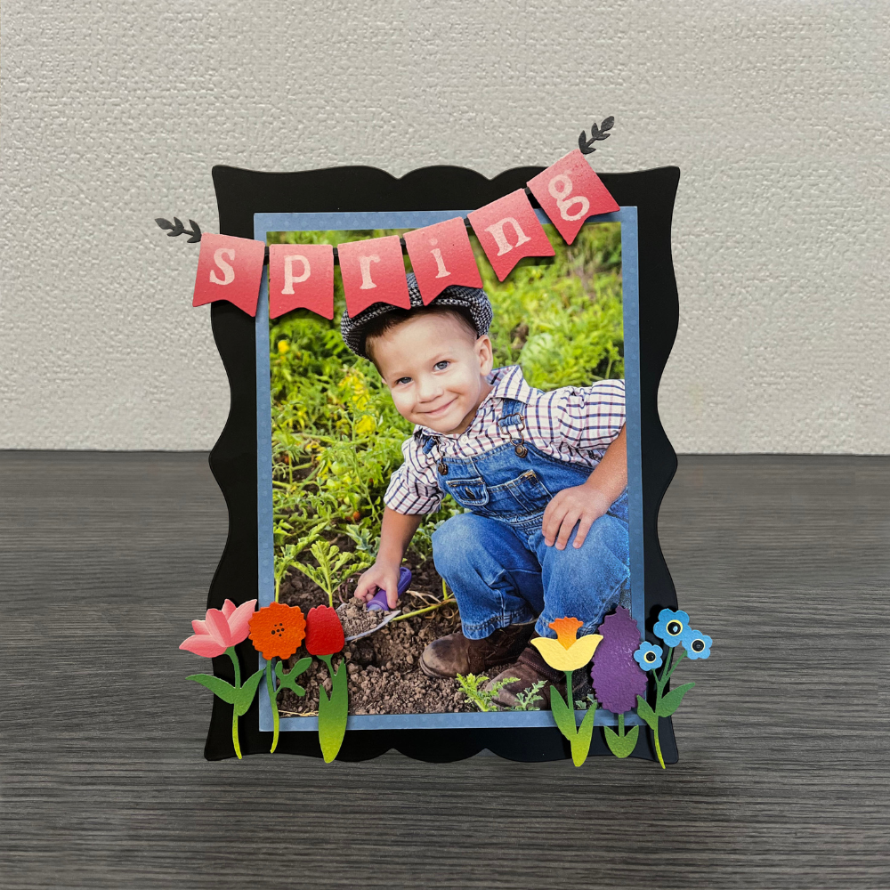 Pink "Spring" Banner magnet on a black easel with flower magnets and a spring picture of a little boy in the garden. 