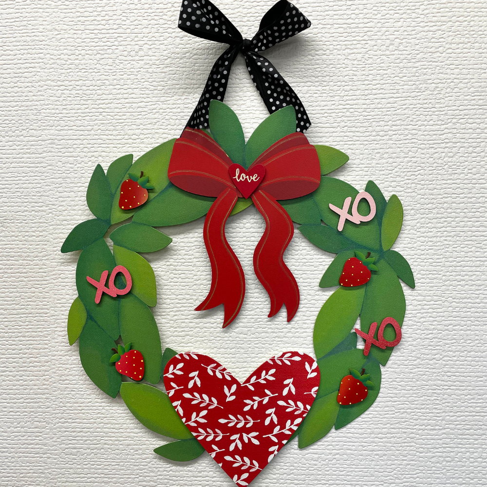 Green leaf wreath with a black ribbon. Decorated with a red ribbon magnet, heart and "xo" magnets and a red and white heart magnet. 