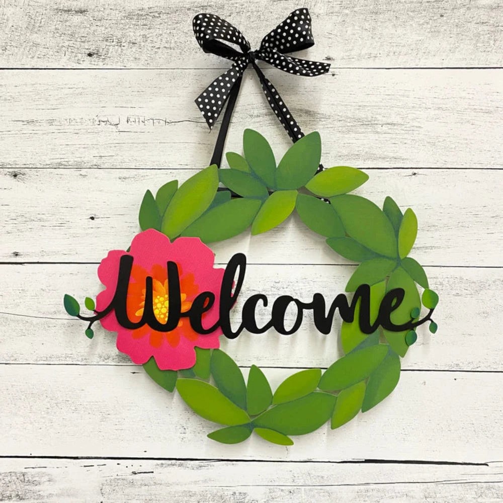 Green Metal wreath hanging from a black ribbon with white polka dots. Welcome magnet and pink flower magnet on wreath. 