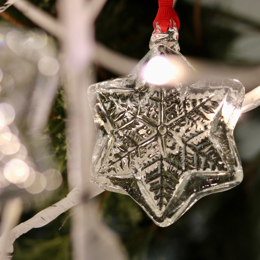 Snow Jewel hanging from a red ribbon from a white tree with white twinkle lights.