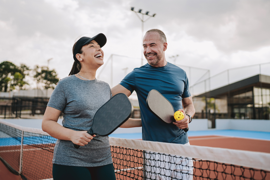 Adults smiling being active on a pickleball court.