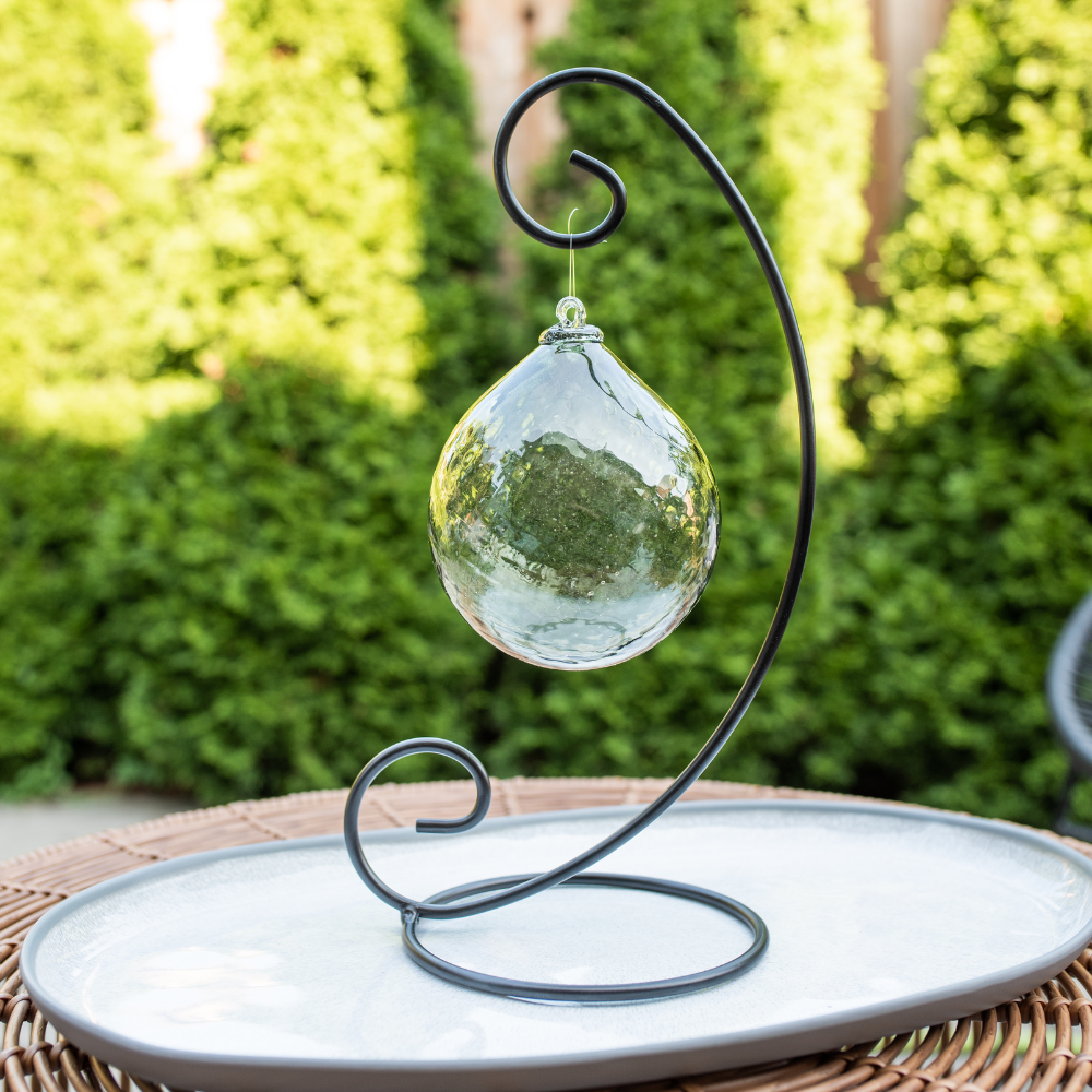 Pewter Enchanting Moonlight Radiance Orb on a Large Curved Single Ornament Holder on a white plate in front of green trees