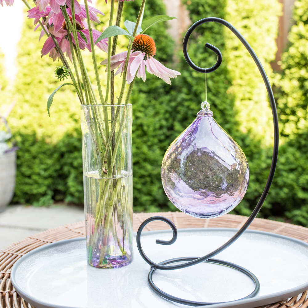 Purple Friendship Vase with pink flowers and Purple Majestic Twilight Radiance Orb on a Large Curved Single Ornament Holder. Displayed on a white plate with green trees in the background