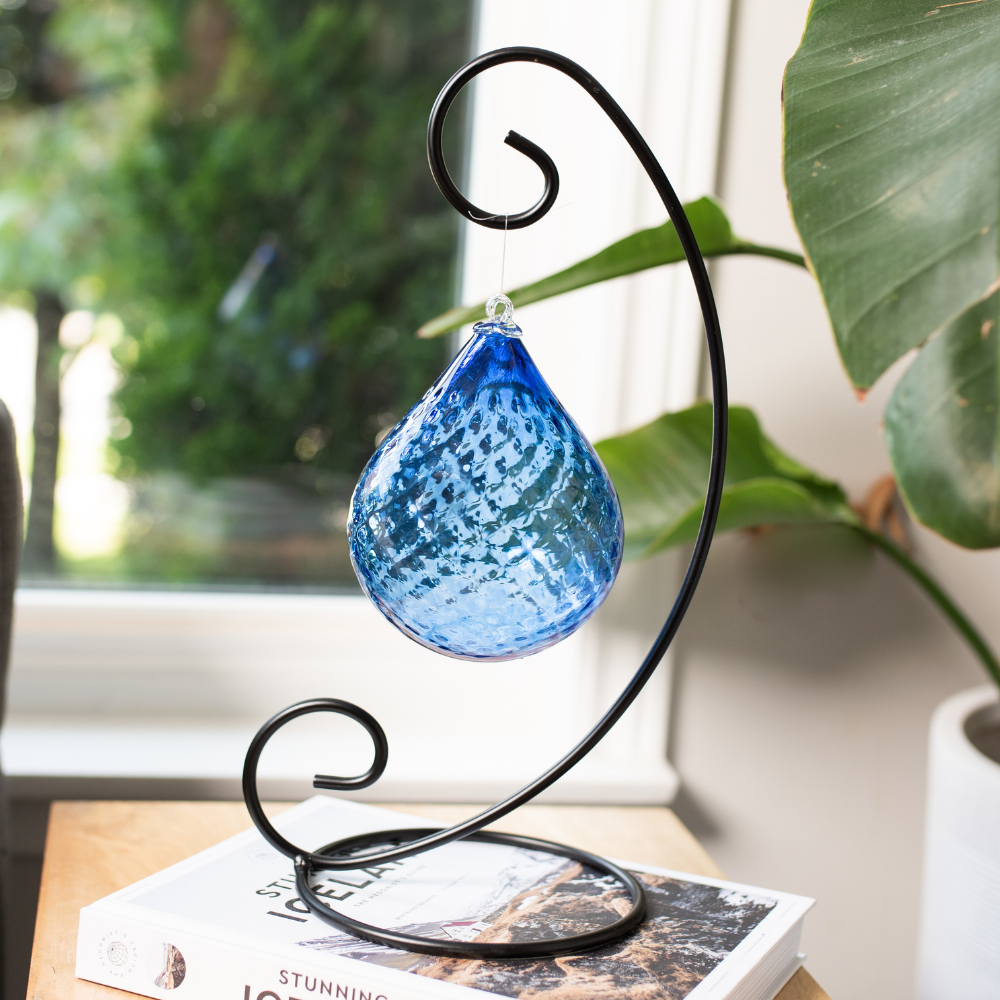 Cobalt Mystical Depths Radiance Orb on a Large Curved Single Ornament Holder on a white book with a window and green plant in the background