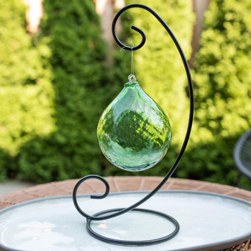 Green Verdant Vitality Radiance Orb on a Large Curved Single Ornament Holder resting on a white plate with green trees in the background