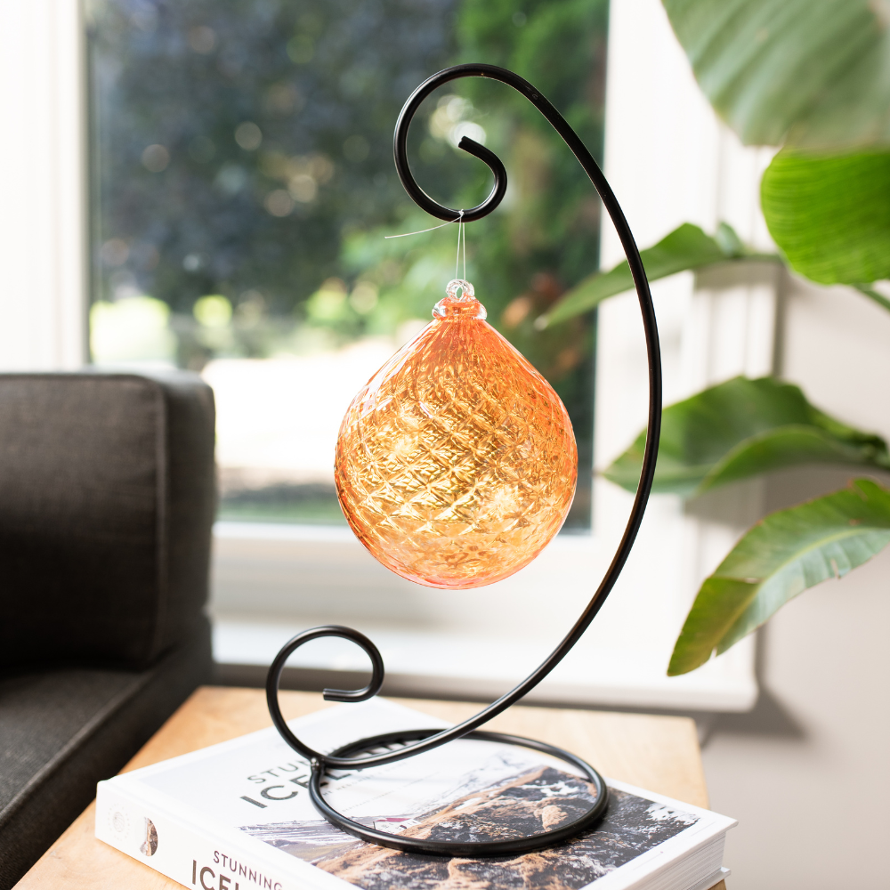 Orange Vibrant Fire Radiance Orb on a Large Curved Single Ornament Holder on a white book on a wood table. Window in the background