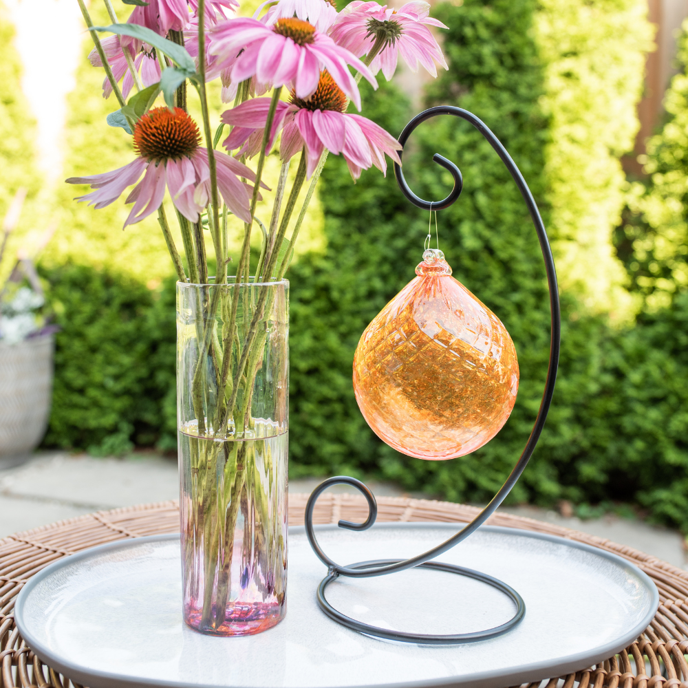 Pink Friendship vase with pink flowers and Orange Vibrant Fire Radiance Orb on a Curved Single Ornament Holder. Displayed on a white tray in front of green trees