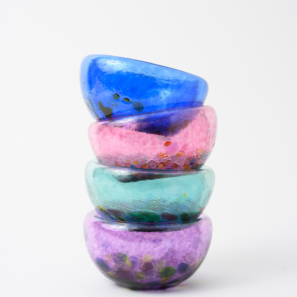 Four blown glass bowls stacked and nested inside one another. From bottom to top: purple with multi-colored spots, teal with multi-coloured spots, pink with multi-coloured spots and blue with multi-coloured spots. 