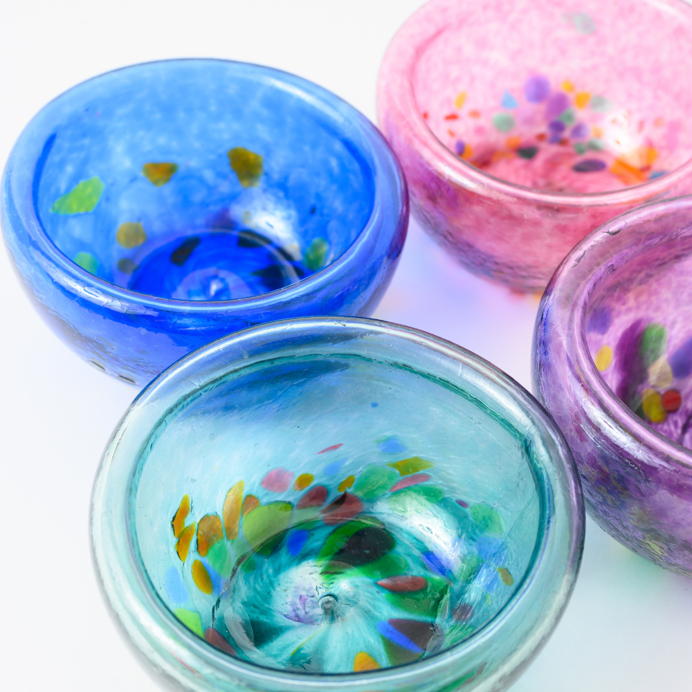 Four blown glass bowls, purple with multi-colored spots, teal with multi-coloured spots, pink with multi-coloured spots and blue with multi-coloured spots. 