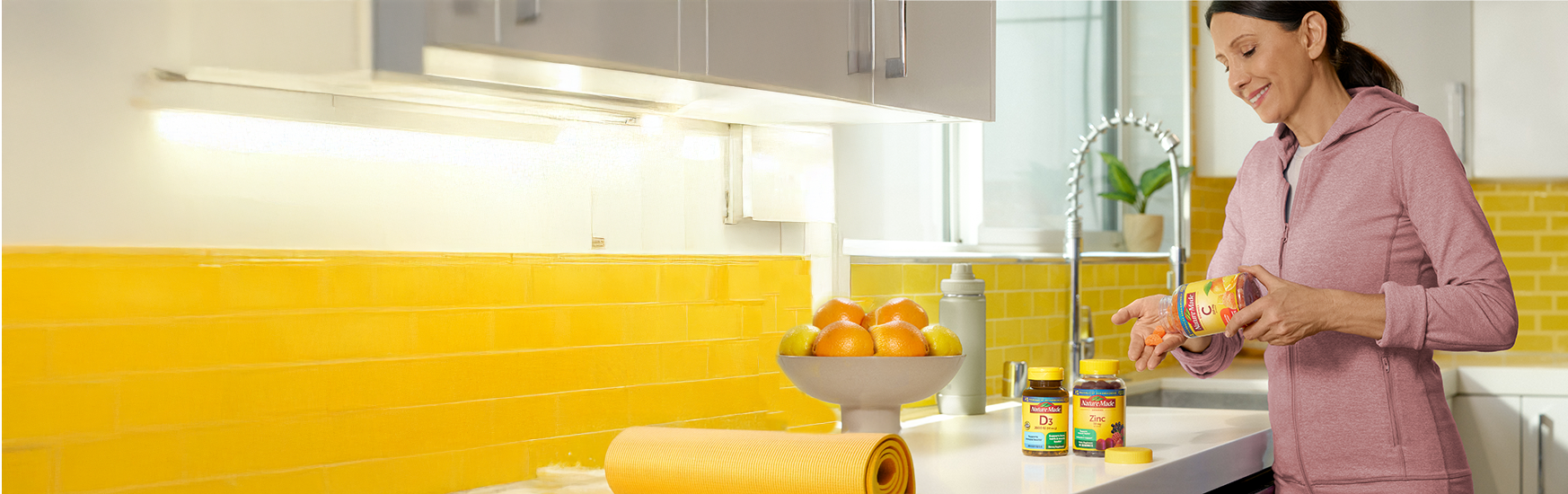 Person holding a bottle of Nature Made Vitamin C immune support supplements, with Vitamin D3 and Zinc bottles and fresh oranges on the counter.