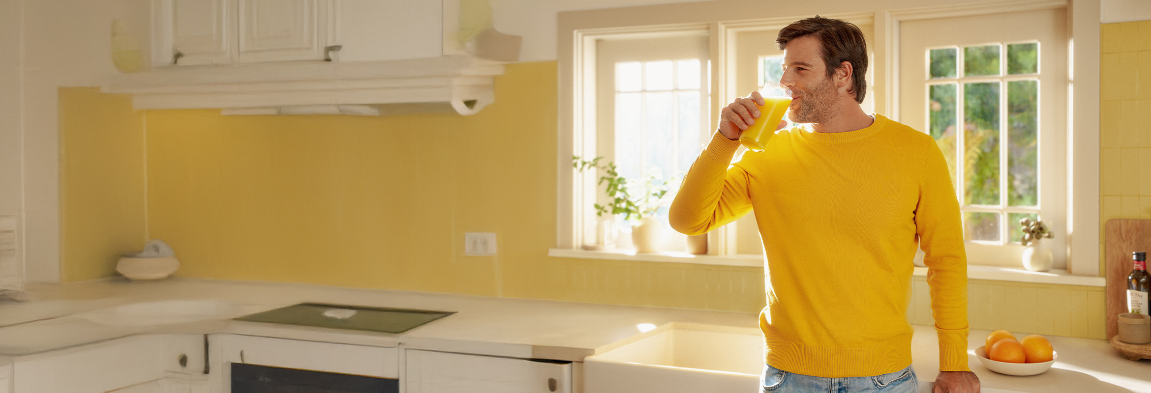 Person in yellow sweater drinking orange juice in home kitchen