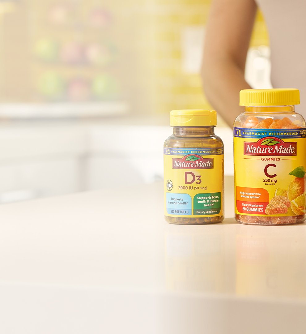 Nature Made immune supplements on a bright kitchen counter with a yellow tile backsplash and a bowl of fresh fruit in the background.