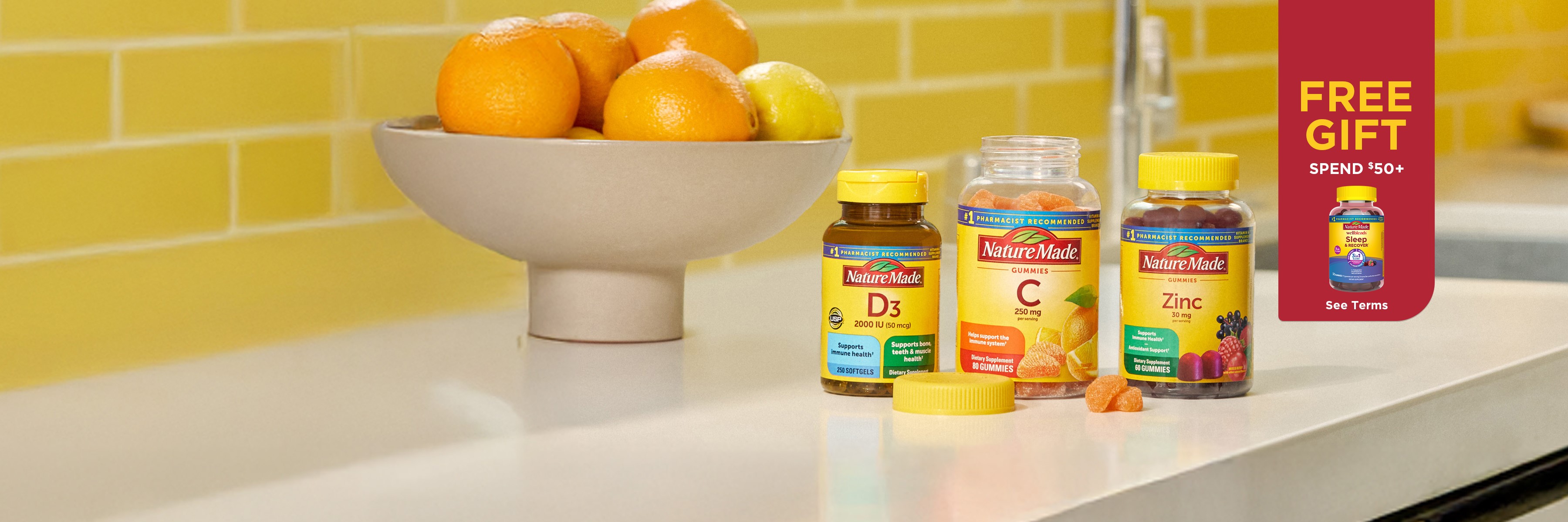 Nature Made Vitamin D3, Vitamin C gummies, and Zinc supplements on a kitchen counter with fresh oranges. Free Gift Sleep & Recover™ Gummies. Spend $50+