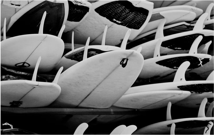 A large collection of stacked surfboards in black and white.