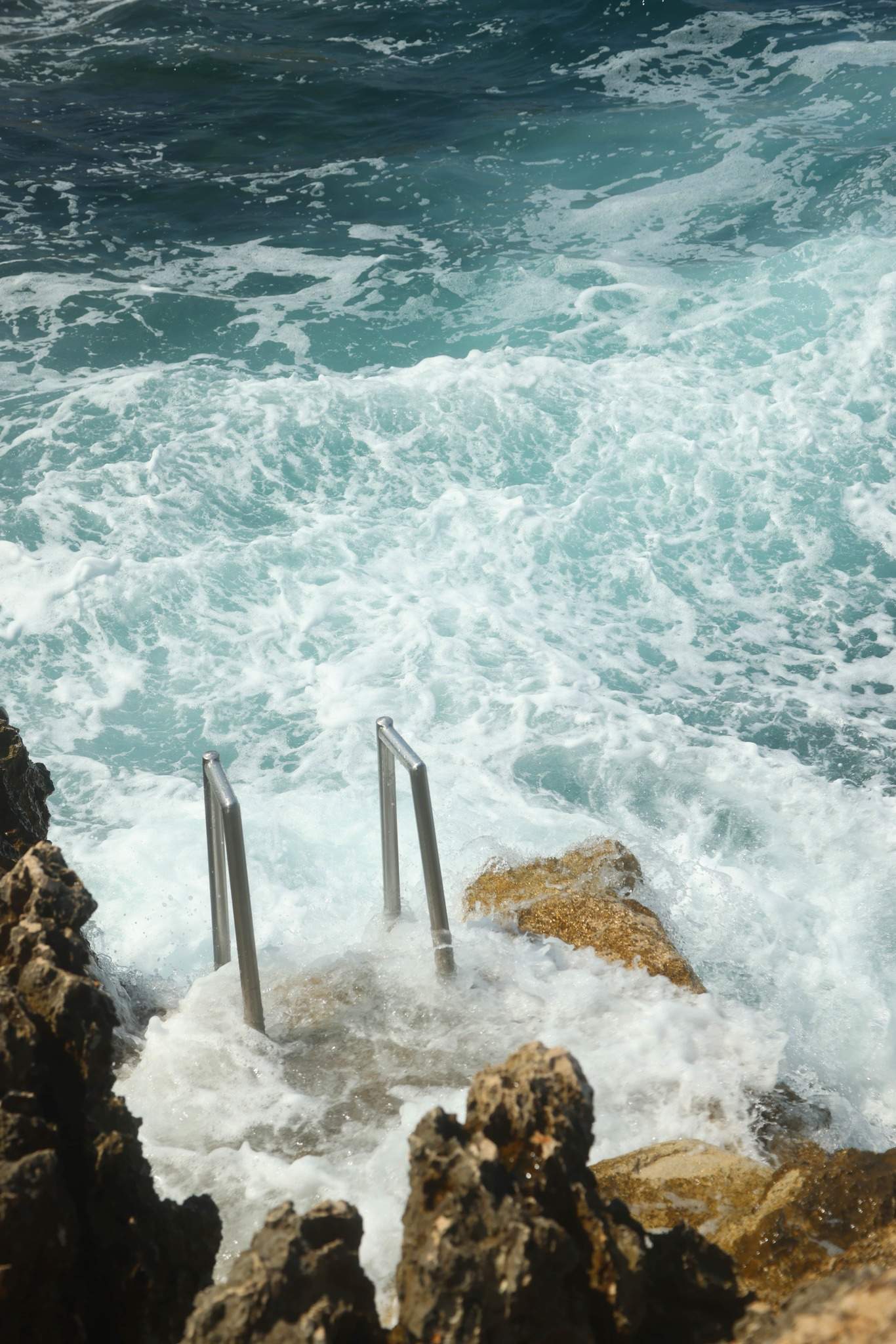 waves crashing onto rocks with ladder into sea