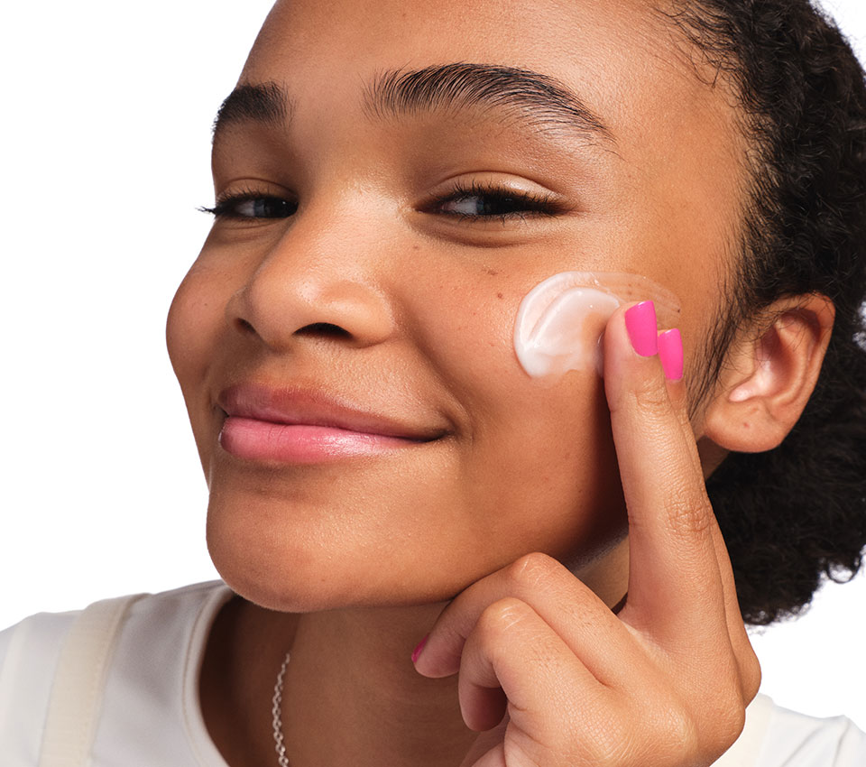 Child applying moisturizer to cheek with a smile.