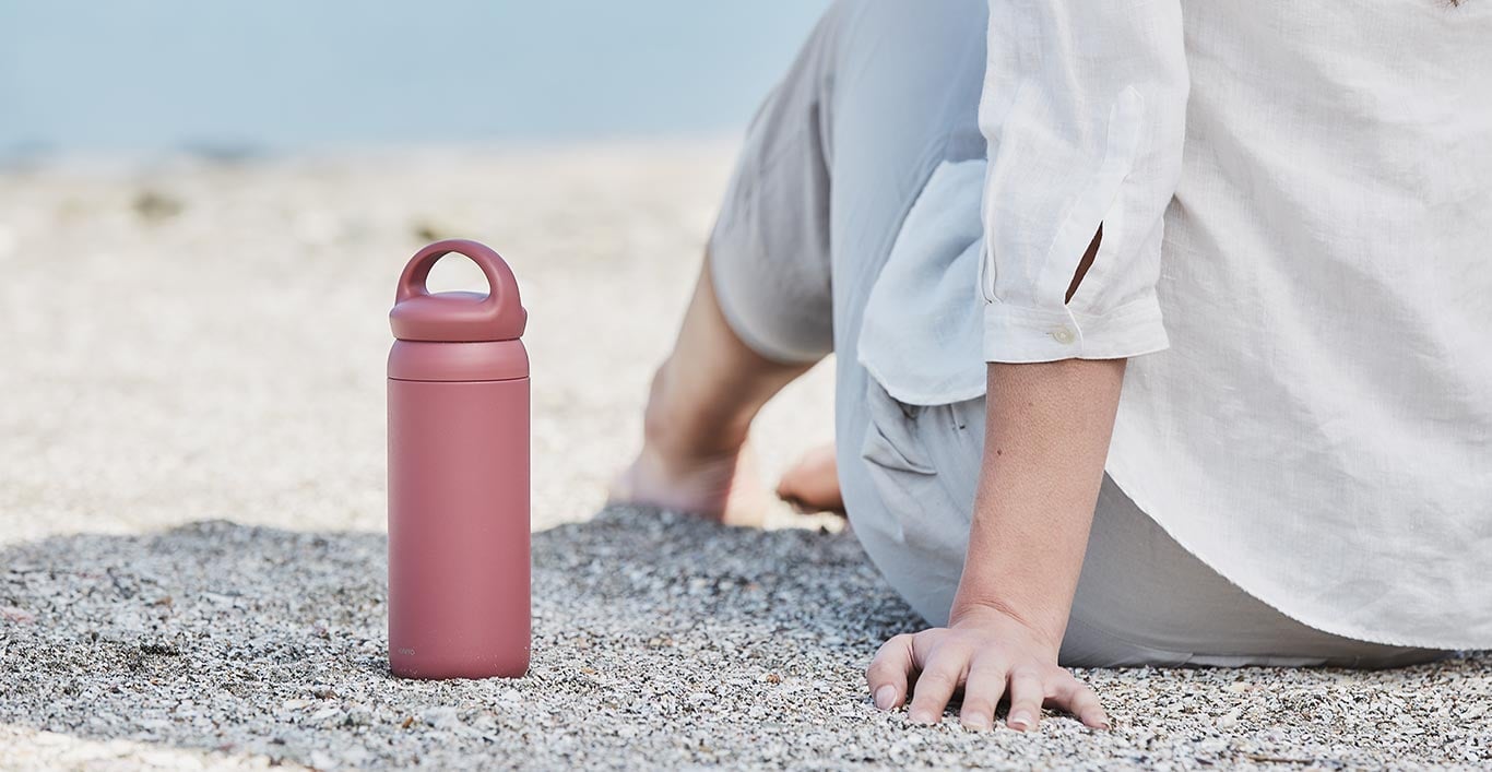 DAY OFF tumbler in rose on next to a person sitting on sand  