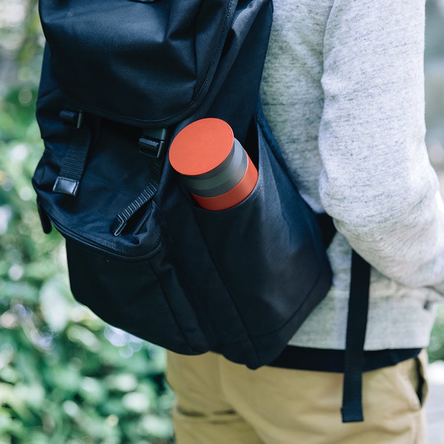  TRAVEL tumbler in red on the side pouch of a backpack  