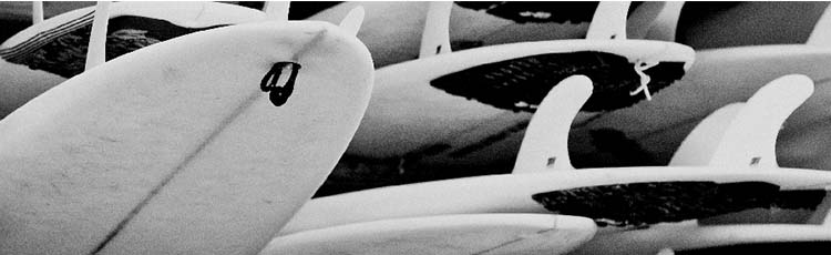 A large collection of stacked surfboards in black and white.