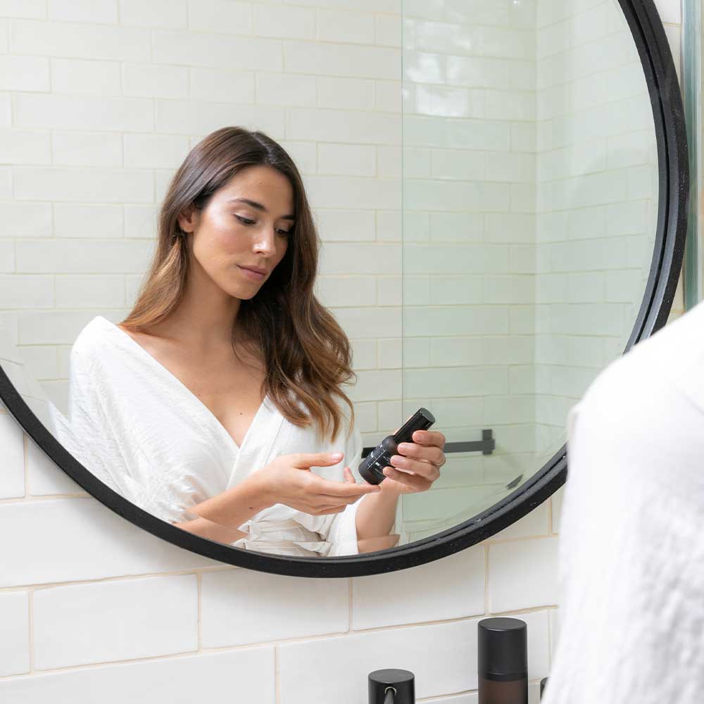Woman applying Synergie Skin serums in her bathroom