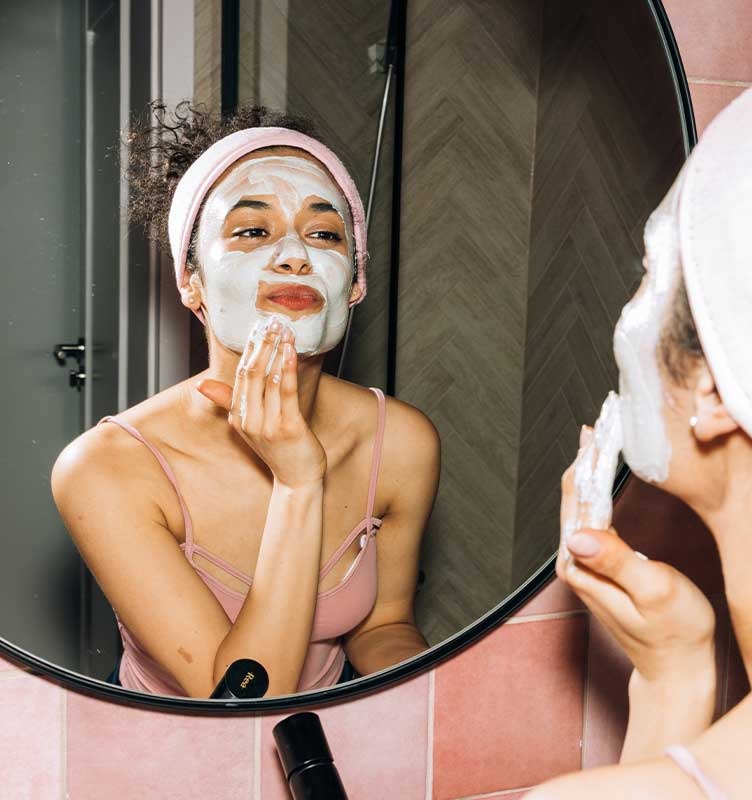 Young woman applying face mask in her bathroom mirror