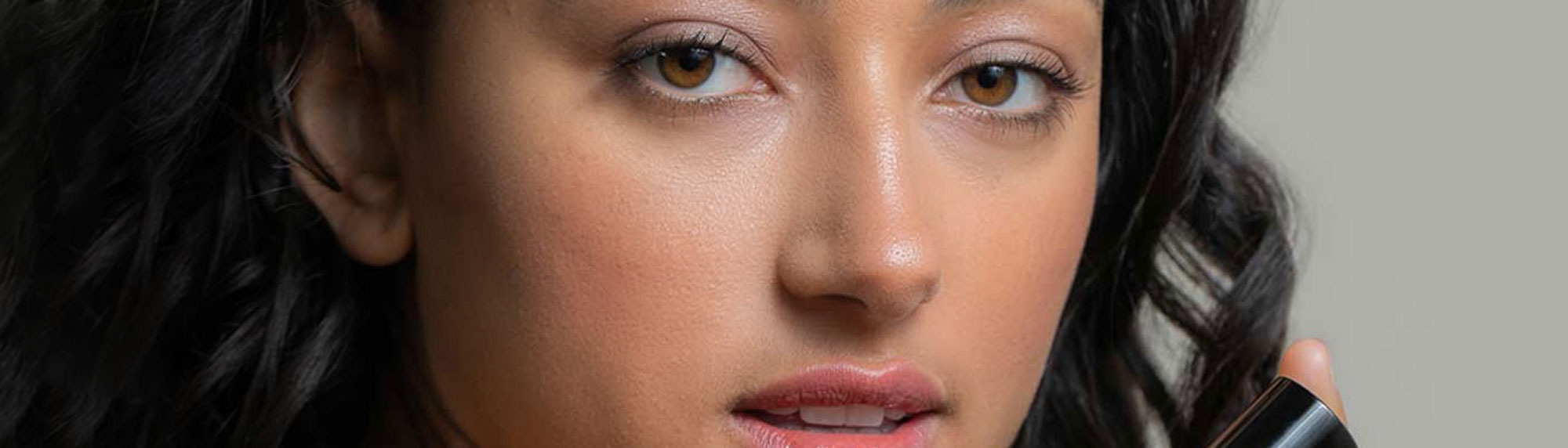 Young woman looking at the camera as she holds a Synergie Skin product