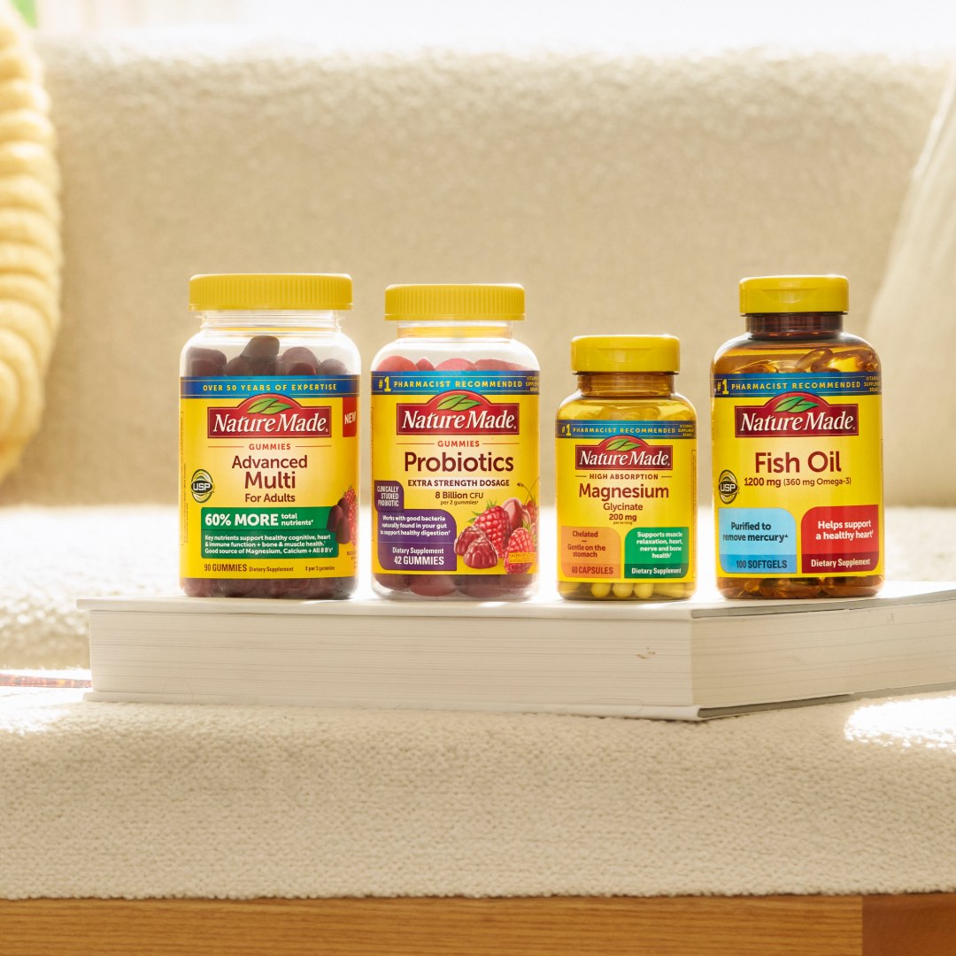 Nature Made vitamins and supplements on a cozy couch with a yellow blanket featuring Advanced Multi, Probiotics, Magnesium, and Fish Oil bottles.