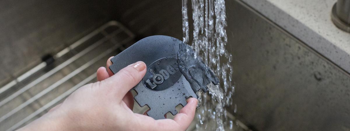 A person cleans the Lodge Grill Pan Scraper in the sink.