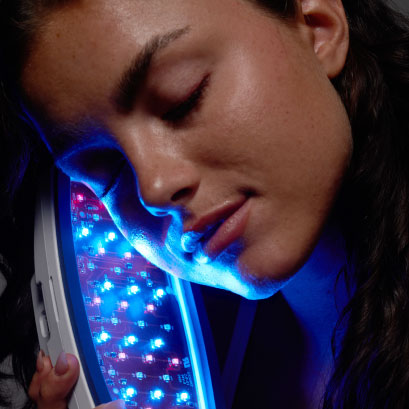 Woman using a blue light therapy handheld LED device for the treatment of acne. 