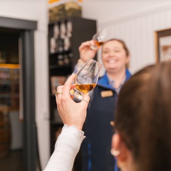A woman taking part in a whisky tasting observing whisky in a Glencairn glass.